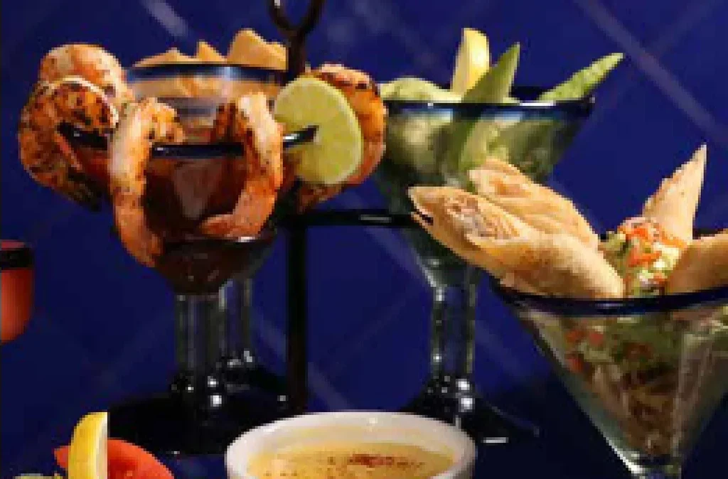 Shrimp cocktail, spring rolls, and green appetizers with sauces on blue.