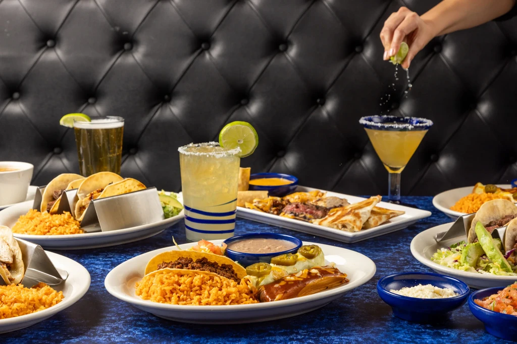 Mexican food and drinks on a table, hand squeezing lime.