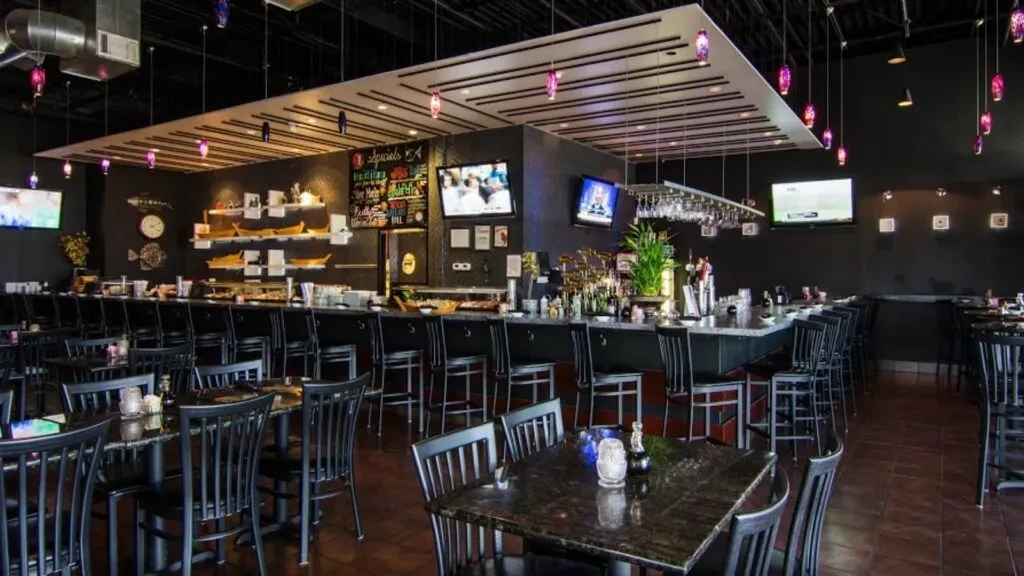 Dark, modern restaurant interior with purple-hued lights, bar, and tables.