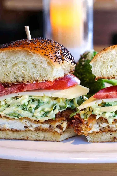 Fried chicken sandwich cut in half, layered with coleslaw and tomato.