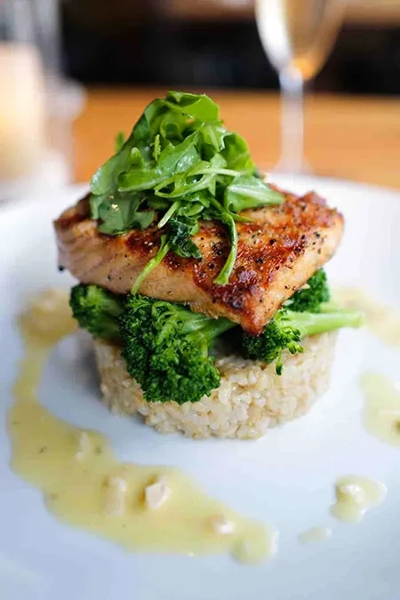 Seared fish, arugula, broccoli, rice, and creamy sauce on white plate.
