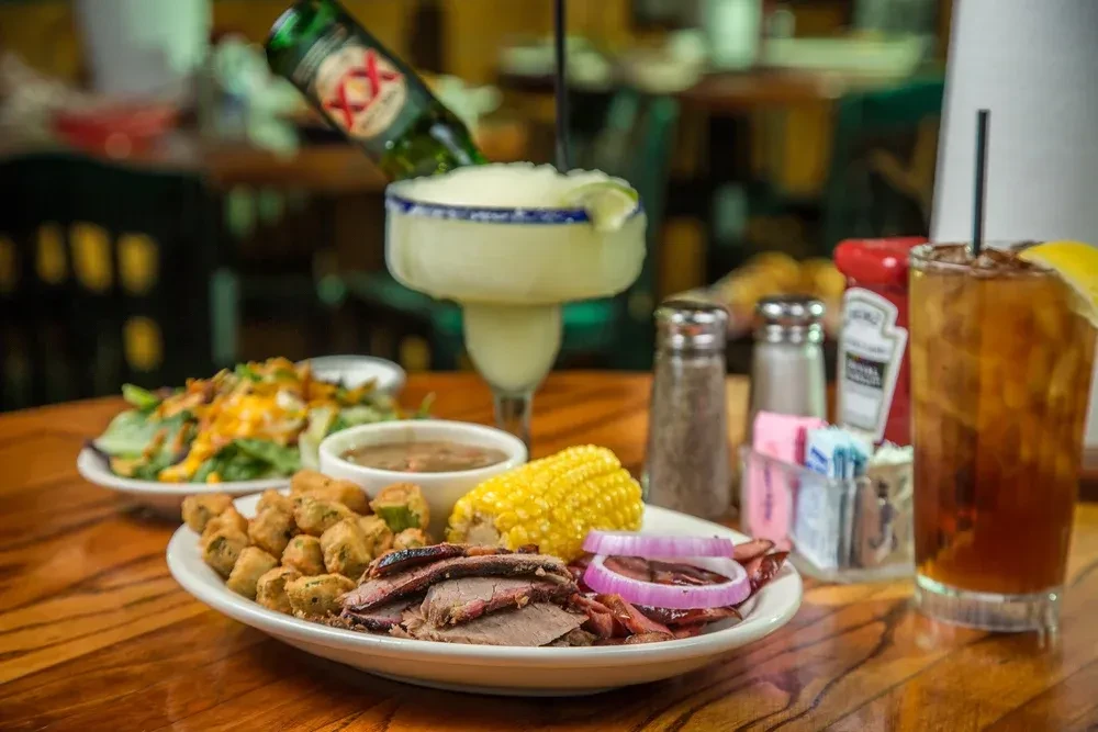 Barbecue plate, salad, iced tea, and beer-rita on a wooden table.
