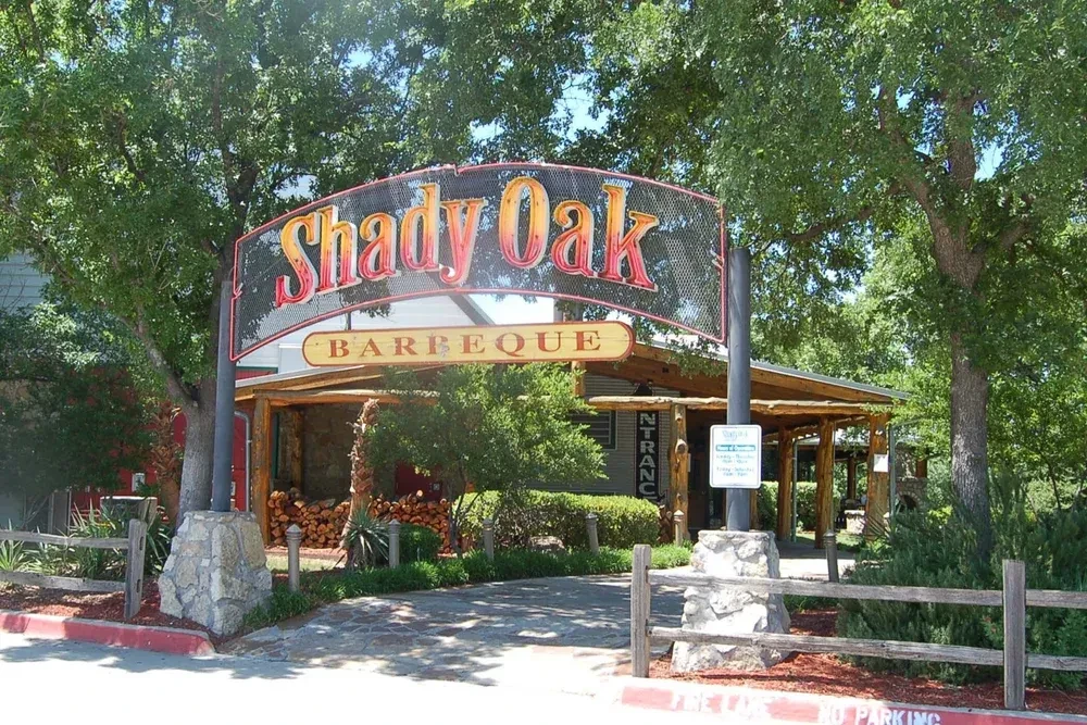 Shady Oak Barbeque restaurant entrance sign, wood pile, rustic setting.