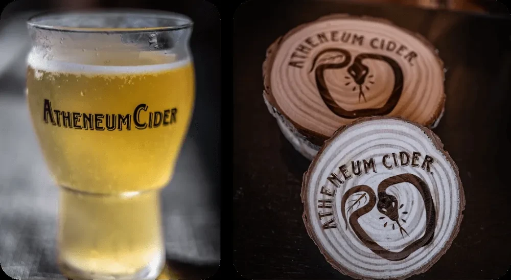 Glass of Atheneum Cider and two engraved wooden coasters.
