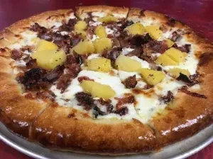 Sliced whole pizza with bacon, pineapple, and cheese on silver pan.