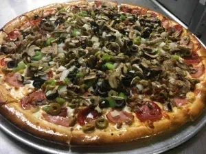 Large round pizza with pepperoni, ham, olives, mushrooms, and veggies.