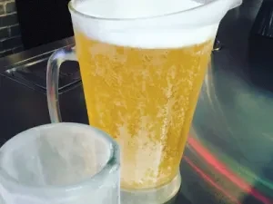 Clear glass pitcher of frothy beer, partial glass visible.