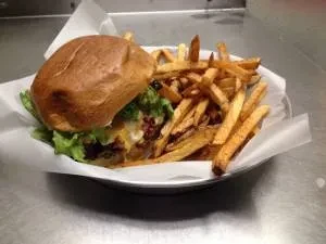 Close-up of a burger, fries, and melted cheese in a white basket.