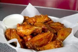 Reddish-brown glazed chicken wings with white dipping sauce in a bowl.