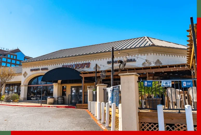 Sunny exterior of Bronco's Sports Grill, showing patio and arched entrance.