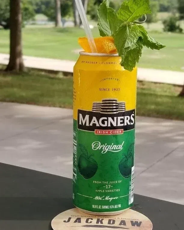 Chilled Magners cider can with straw, orange peel, and mint outdoors.