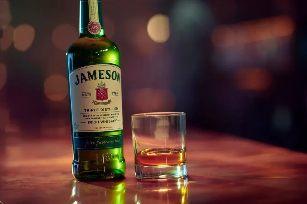 Green Jameson whiskey bottle and glass of amber liquid on a bar.