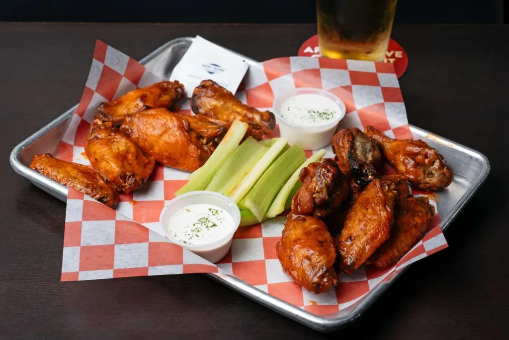 Crispy buffalo wings, celery, and dip on a checkered tray.