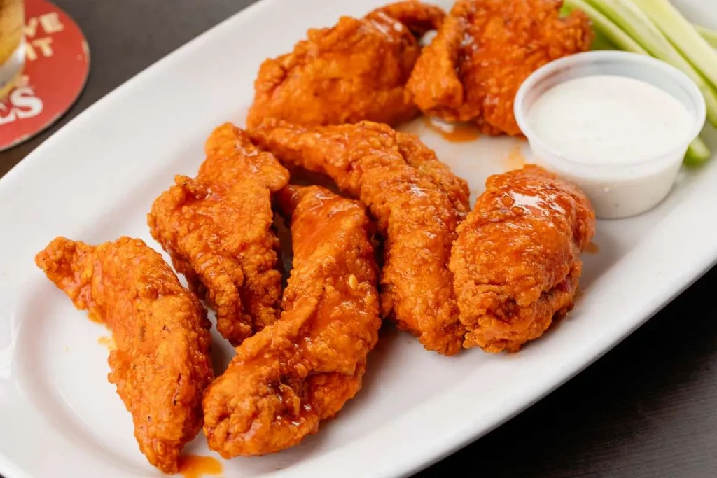 Plate of boneless buffalo chicken tenders with celery and dip.