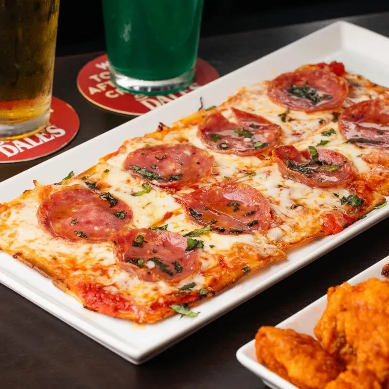 Pepperoni flatbread pizza, chicken wings, beer, and a green drink.