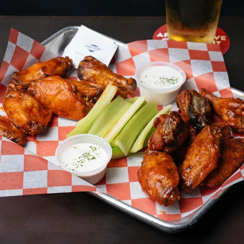 Saucy buffalo wings, celery, and dips on a tray, with a beer.