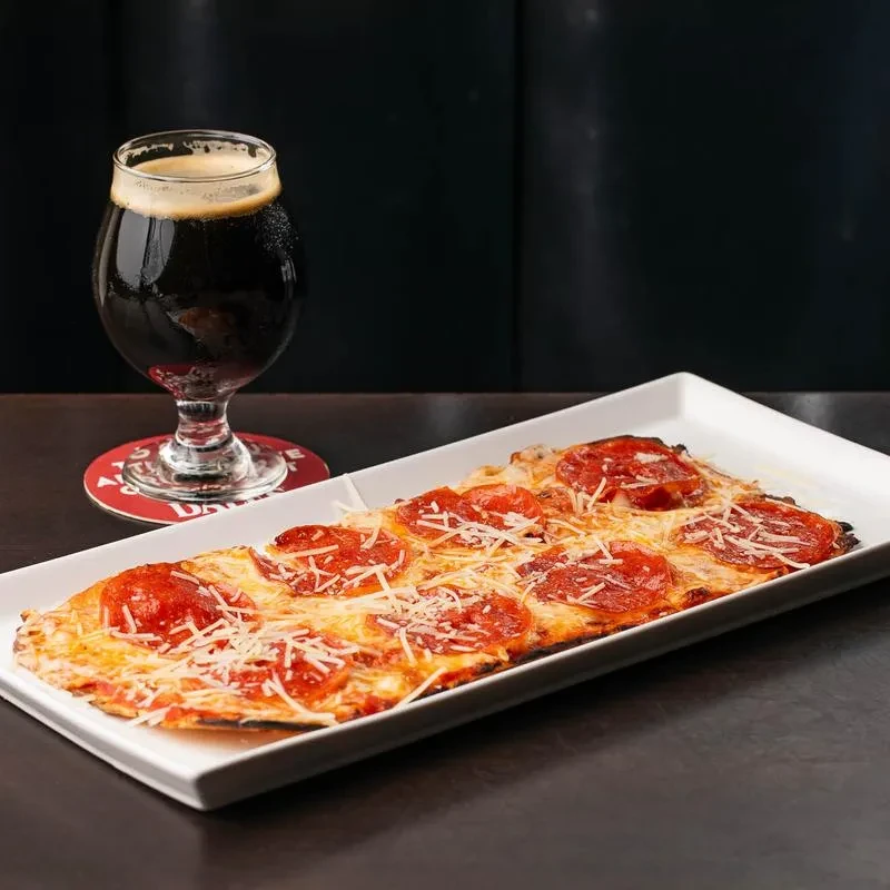 Pepperoni flatbread pizza with melted cheese, served with a dark beer.