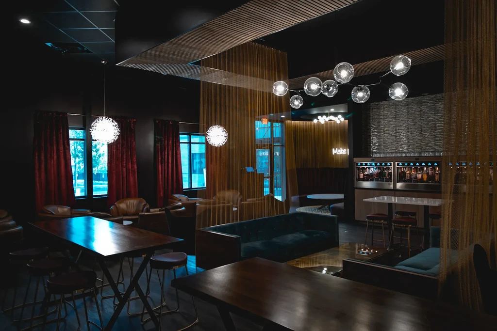 Moody bar lounge with red curtains, chandeliers, and beverage dispensers.