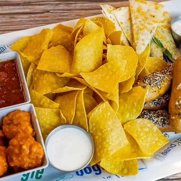 Platter of tortilla chips, salsa, orange chicken, quesadilla slices, and breadsticks.
