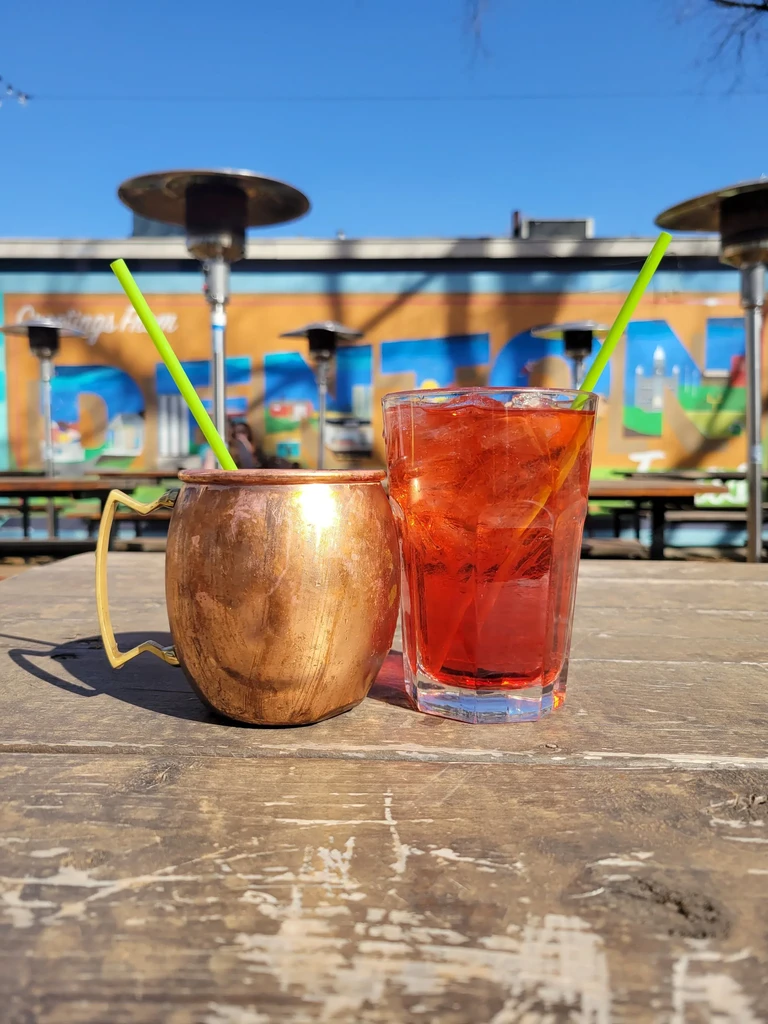 Drinks on a wooden table with a 'Greetings from' mural backdrop.