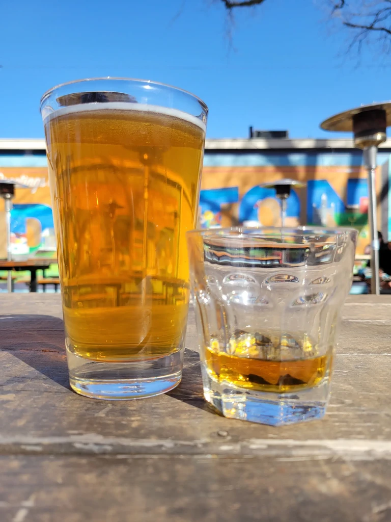 Beer and whiskey on a rustic wooden table in sunlight.