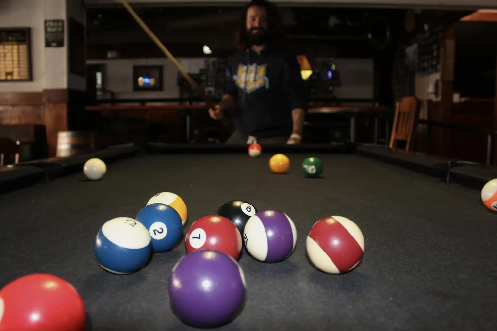 Scattered colorful pool balls on a table, blurred person with cue.
