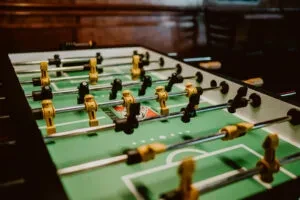 Close-up of a foosball table's green field, players, and blurred wooden background.