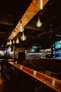 Long polished wooden bar with hanging Edison bulbs in a dim interior.
