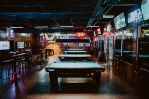 Moodily lit pub with many pool tables, high-tops, and neon signs.
