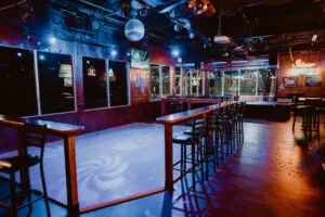 Empty club interior with a blue-purple dance floor, disco ball, and bar.