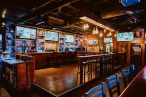 Long, well-stocked, dimly lit sports bar with beer taps and screens.