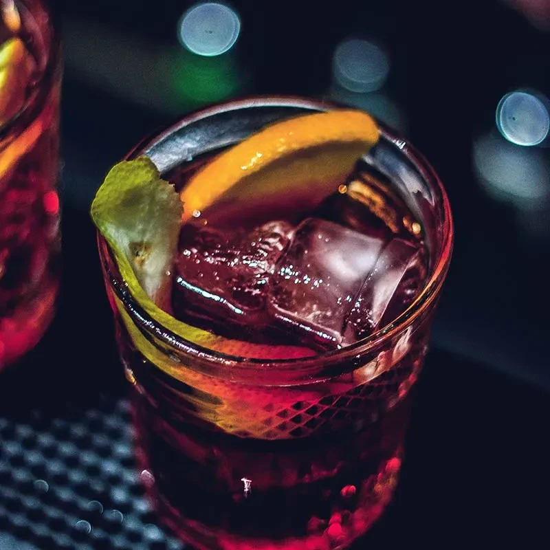 Reddish-purple cocktail in textured glass, with ice, orange, and citrus.