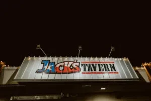 Illuminated "JACK'S TAVERN" sign at night with Texas flag design.
