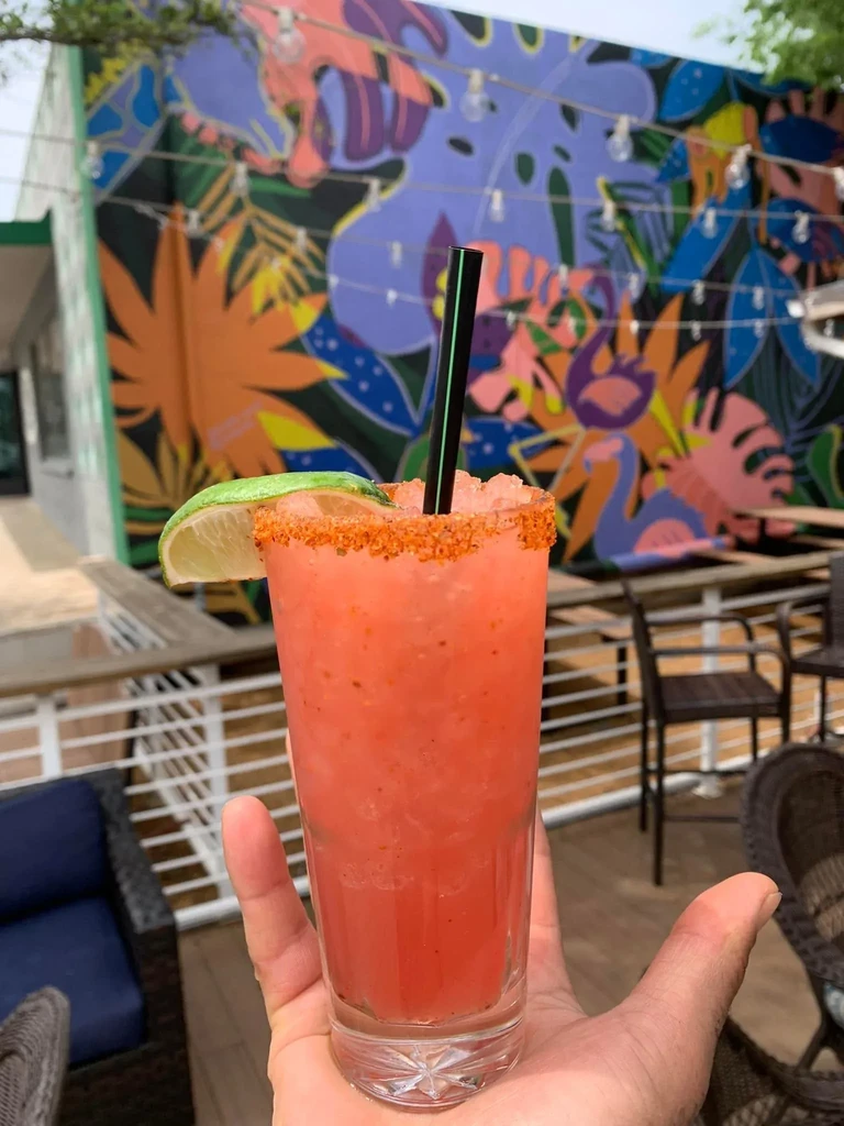 Pink slushy drink with lime, chili rim, held on a patio.