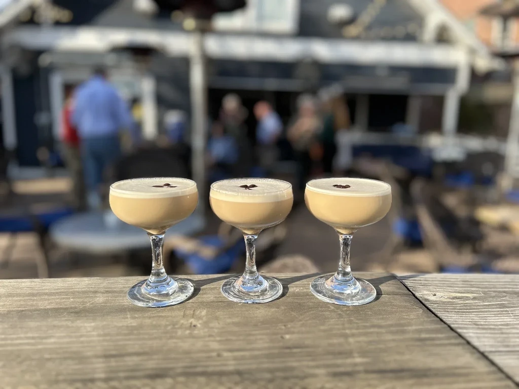 Three identical espresso martinis with foam on a rustic wooden table.