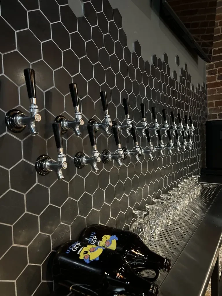 Black tiled bar wall with chrome beer taps and d20 Tavern bottles.