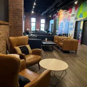 Modern lounge with tan leather armchairs, marble tables, and a colorful mural.