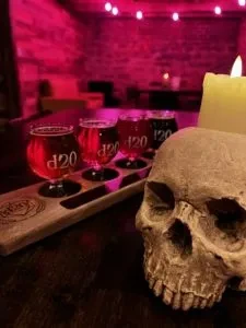 Decorative skull, lit candle, d20 beer flight, magenta brick wall.