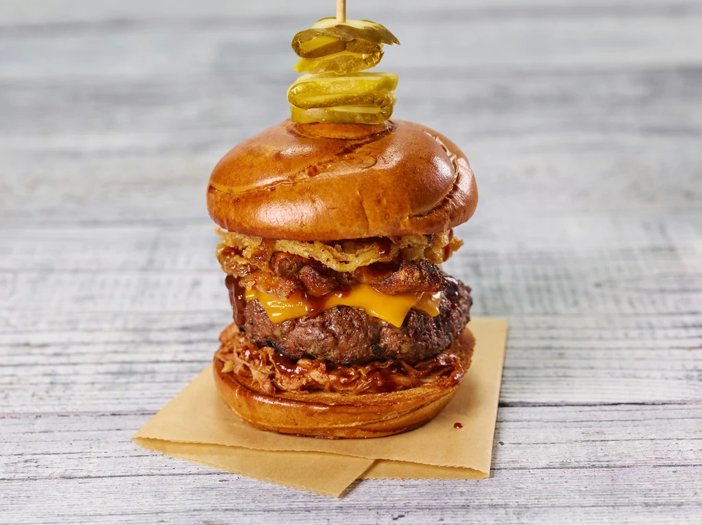 Close-up gourmet burger with beef, melted cheese, bacon, onion rings, and pickles.
