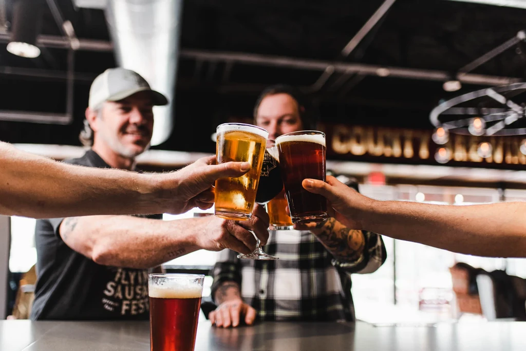 Four hands toasting three beer glasses in a bar or brewery.
