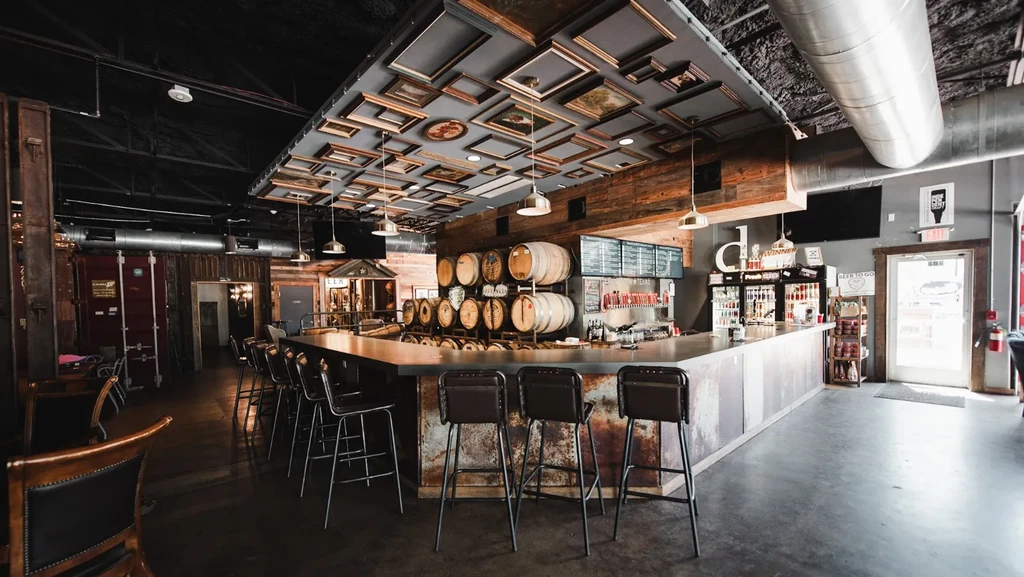 Warmly lit industrial bar with corrugated counter, barrels, and distinctive ceiling.