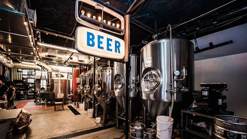 Craft brewery interior with large steel tanks and an illuminated BEER sign.