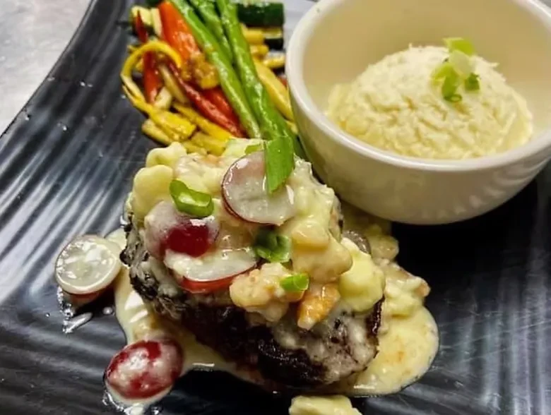 Seared main with creamy sauce, grapes, colorful vegetables, and mashed potatoes.