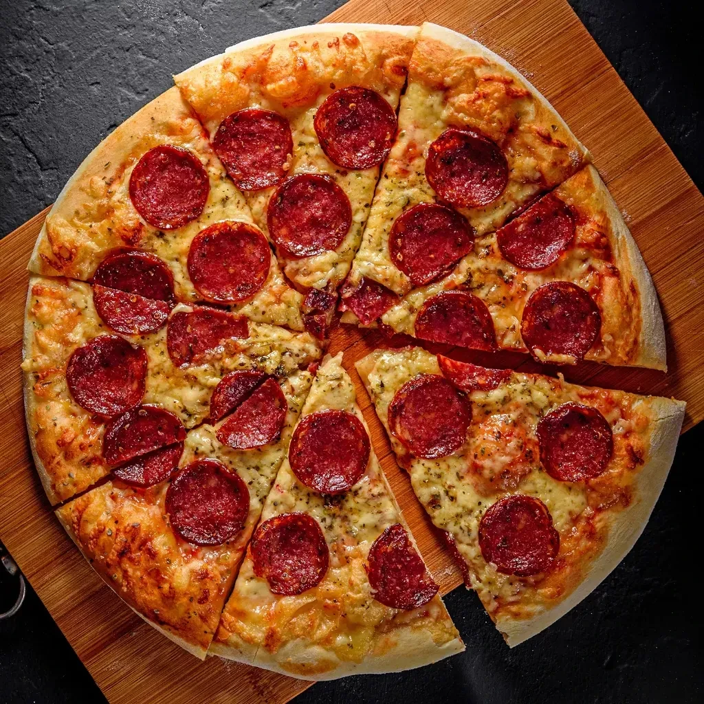 Sliced pepperoni pizza with melted cheese and herbs on a wooden board.