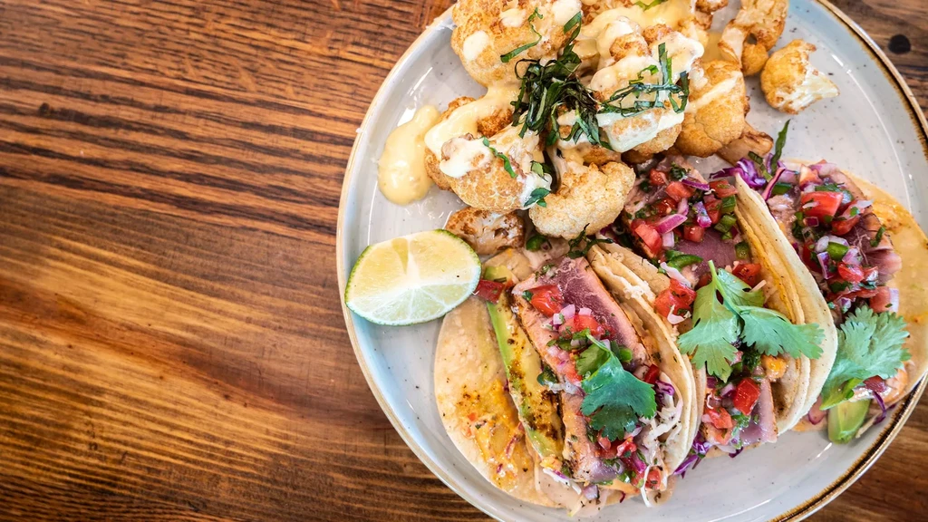 Three fish tacos, roasted cauliflower, and lime on a rustic plate.