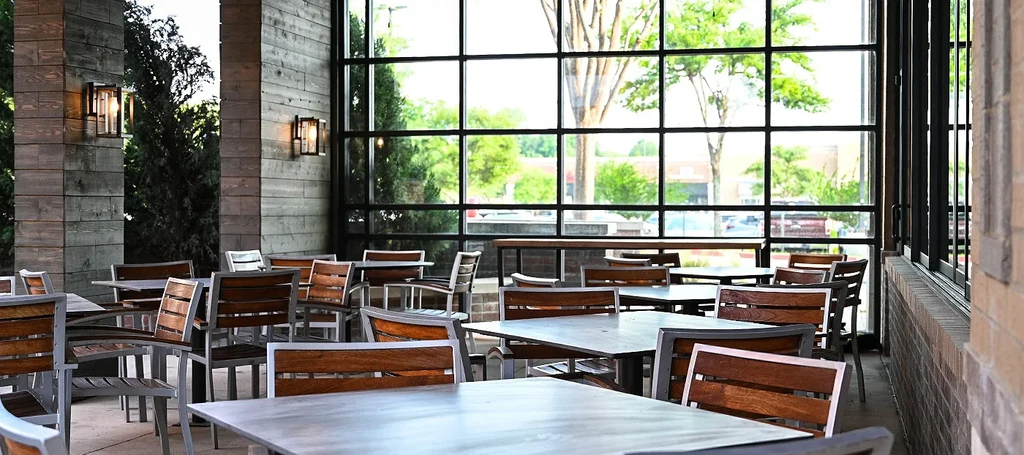Empty modern restaurant dining area with wood pillars and large windows.