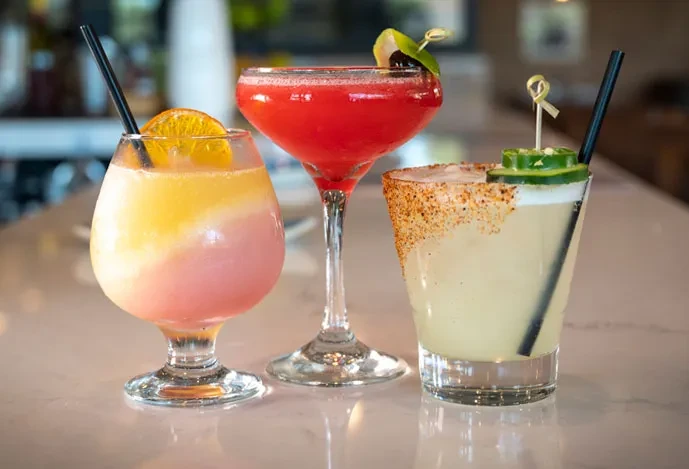 Three colorful cocktails: layered, red, and spice-rimmed with jalapeños.