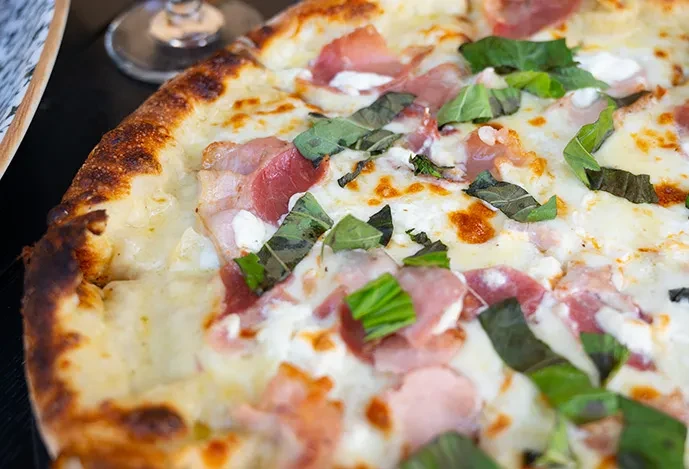 Freshly baked pizza with melted cheese, prosciutto, and basil leaves.