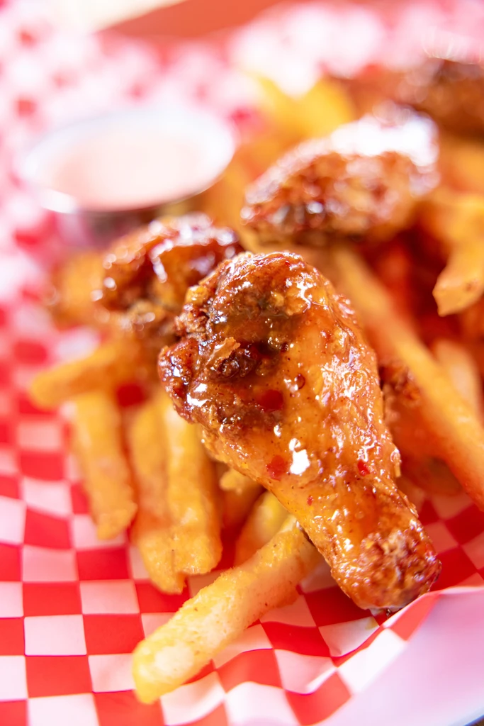 Close-up of crispy glazed chicken wings, fries, and dipping sauce.
