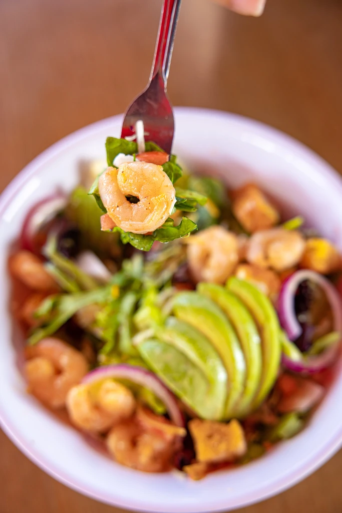 Hand lifts shrimp and fresh greens from a colorful salad bowl.